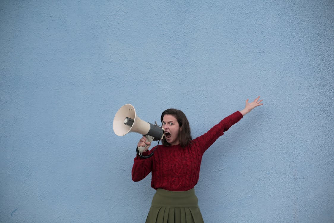 Woman shouting through a megaphone against a blue wall, symbolizing customer complaints or criticism related to TurboDebt services.