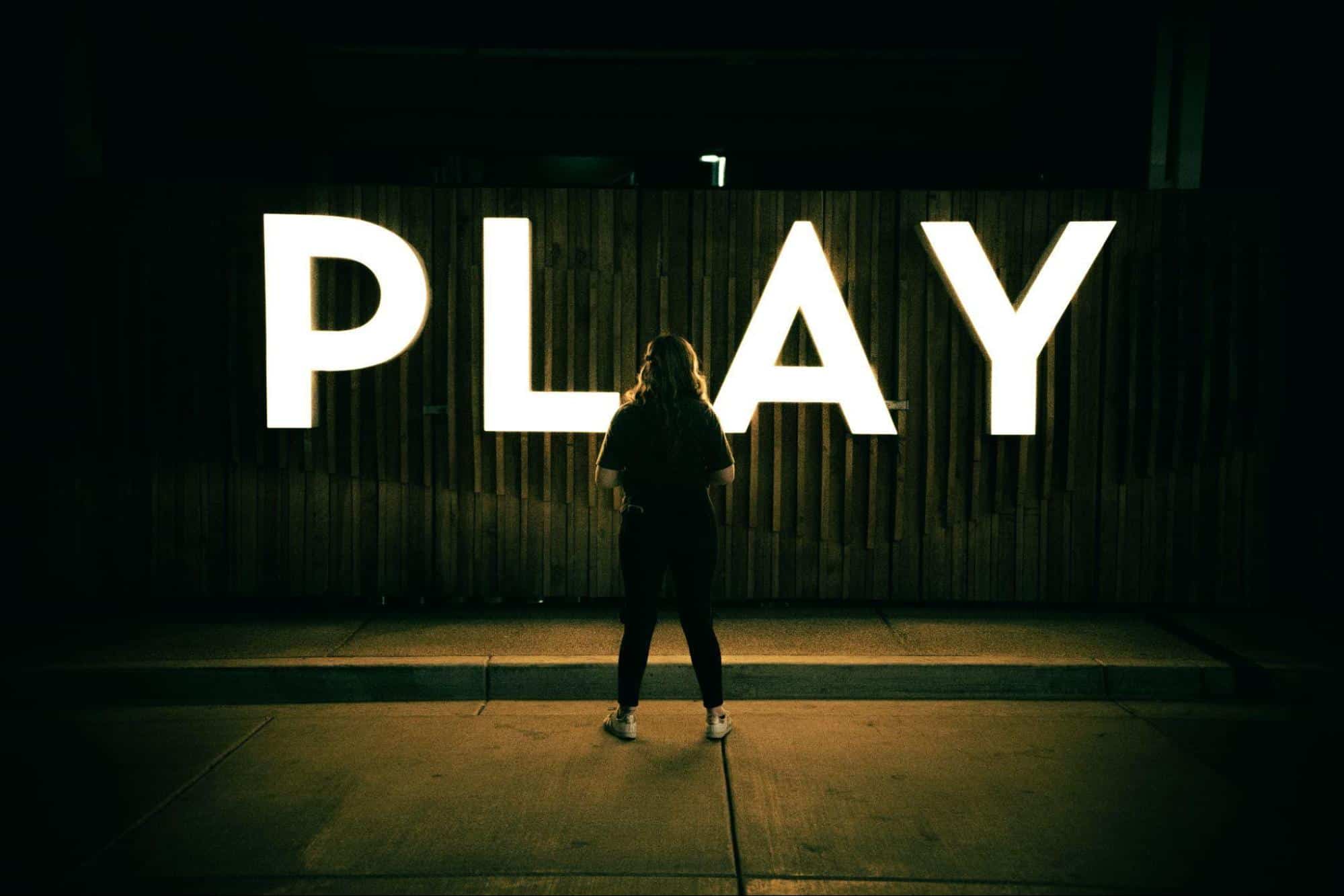 A person standing in front of a large illuminated sign that spells out "PLAY," symbolizing entertainment and the theme of responsible gambling.