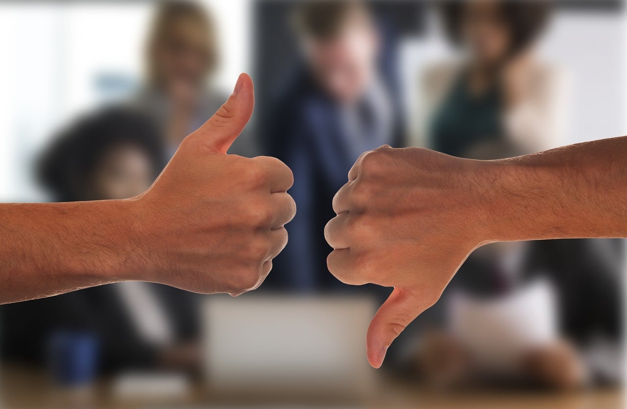 Two hands giving thumbs up and thumbs down in front of a blurred business meeting background, representing the pros and cons of using CreditFresh.