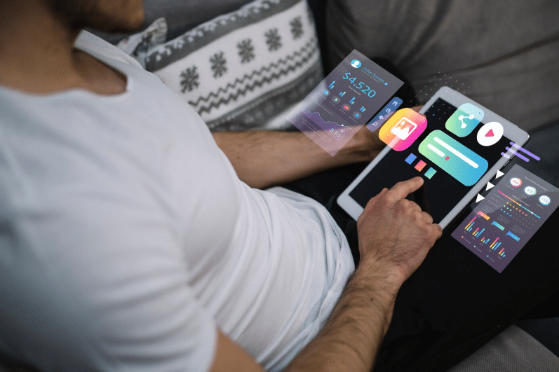 A man using a digital tablet that displays floating 3D icons for likes, shares, and video plays, alongside data charts representing social media engagement metrics.
