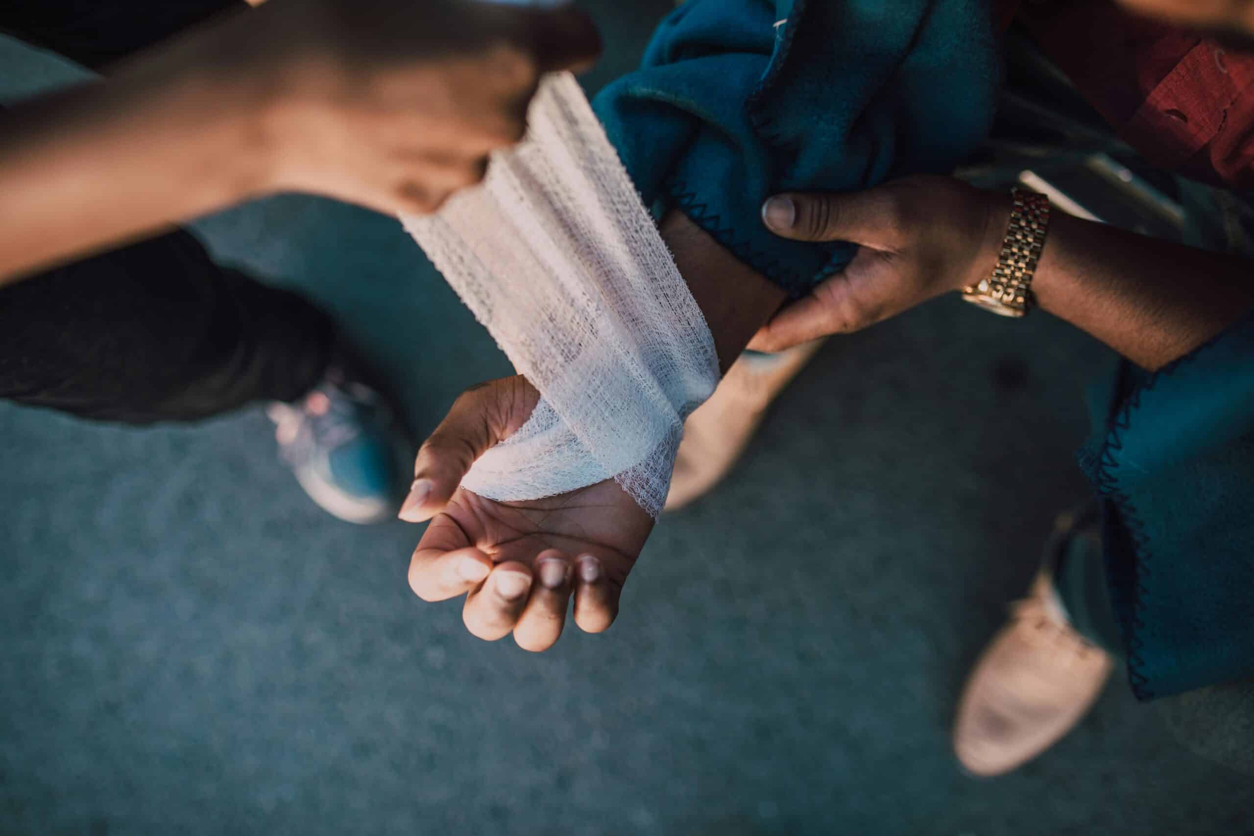 A close-up, overhead view of one person wrapping a white gauze bandage around another person’s wrist and hand.