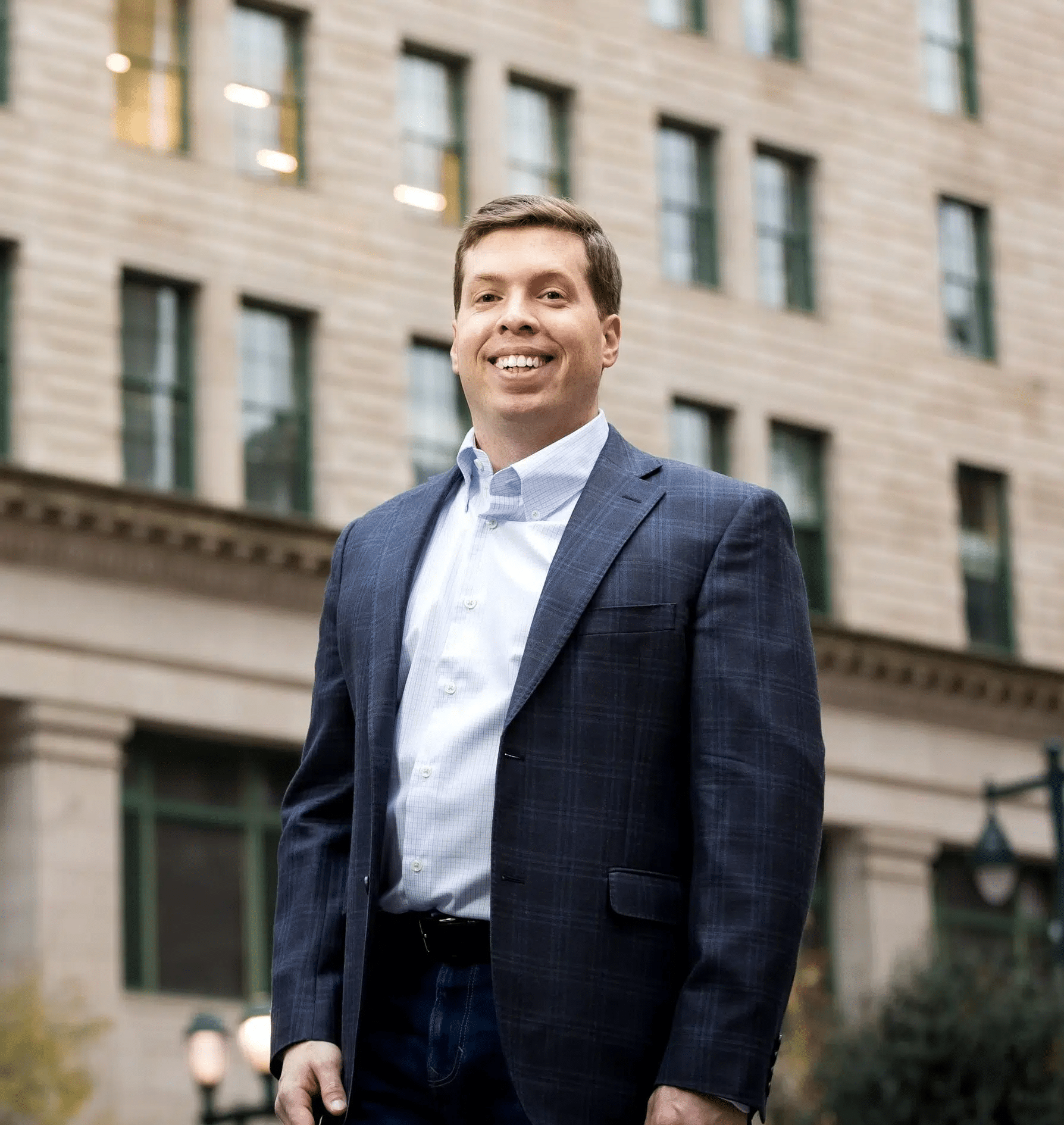Professional headshot of attorney Daniel H. Weberman smiling in a navy plaid blazer and light blue shirt in front of a New York City building.
